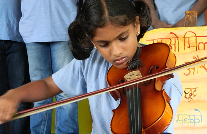 Close-up of a young girl playing a violin while others stand in the background.