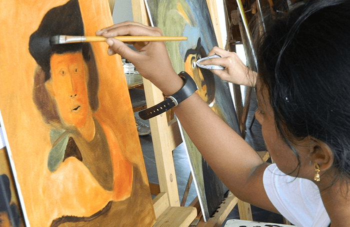 A student holds a brush, dabbing paint on canvas placed on an easel.