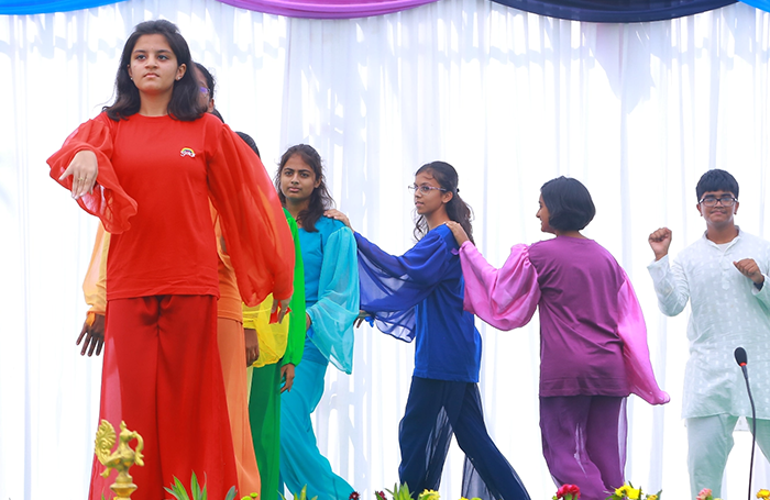 A group of children wearing rainbow colours move on a stage in a Eurythmy performance.