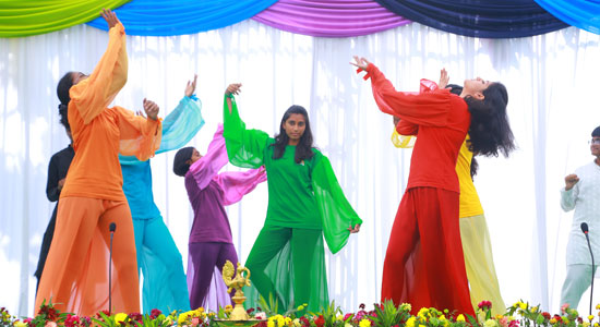 Students wearing rainbow-coloured garments move together on stage in a Eurythmy performance at Sloka.