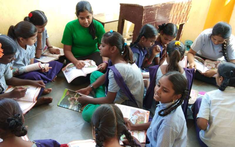 A sloka student sits among a group of students of another school as part of a community service project.