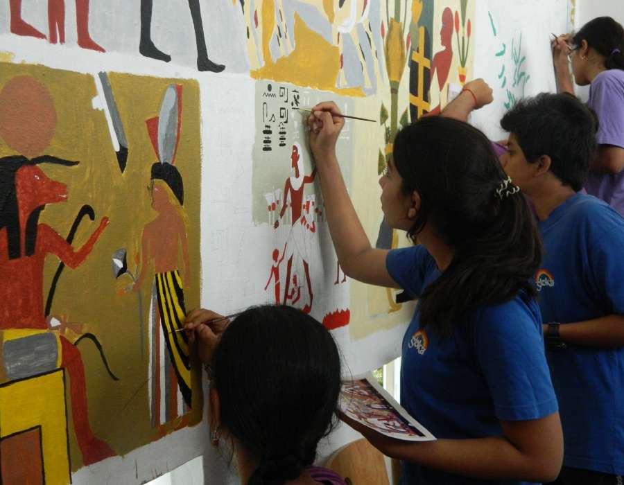 Students of Sloka painting Egyptian-style murals on a wall.