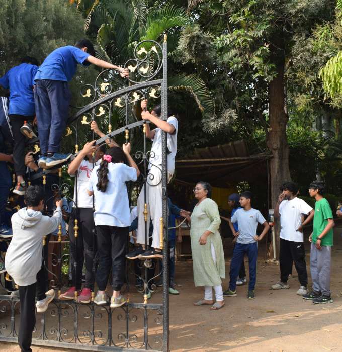 Students climb up on a gate, while others cluster around in the background.