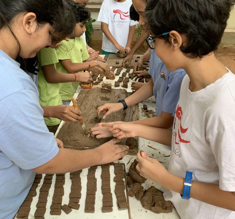Children stand on either side of a bench working hands-on with chunks and blocks of clay.