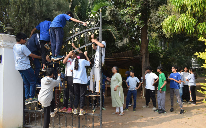7-8 students climb on a gate while others stand clustered in the background.