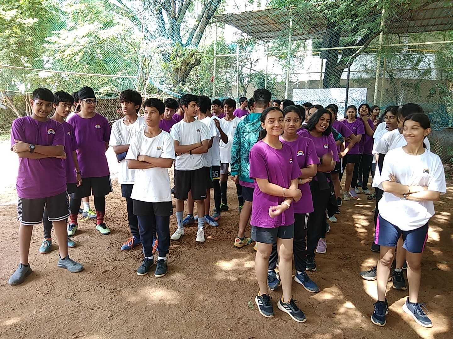 Several students of Sloka - The Hyderabad Waldorf School dressed in purple and white T-shirts stand in rows on a playground.