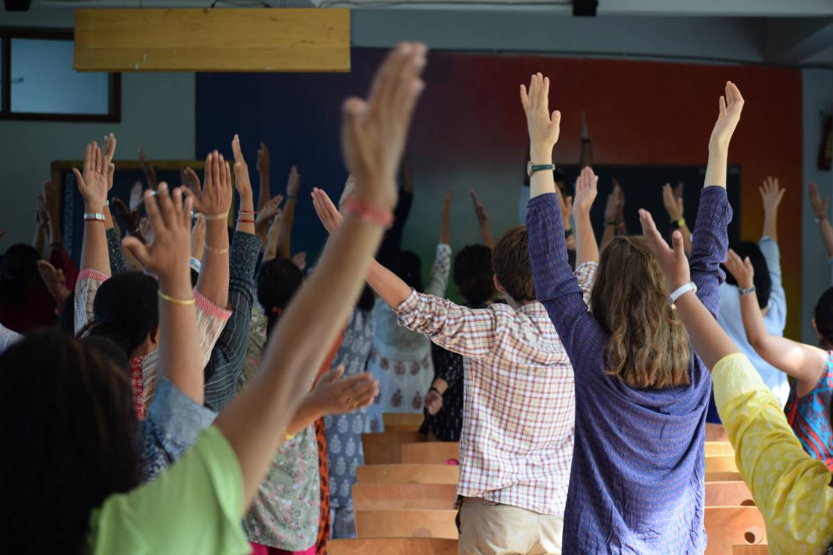 Several people stand in a classroom, raising both arms in the air.