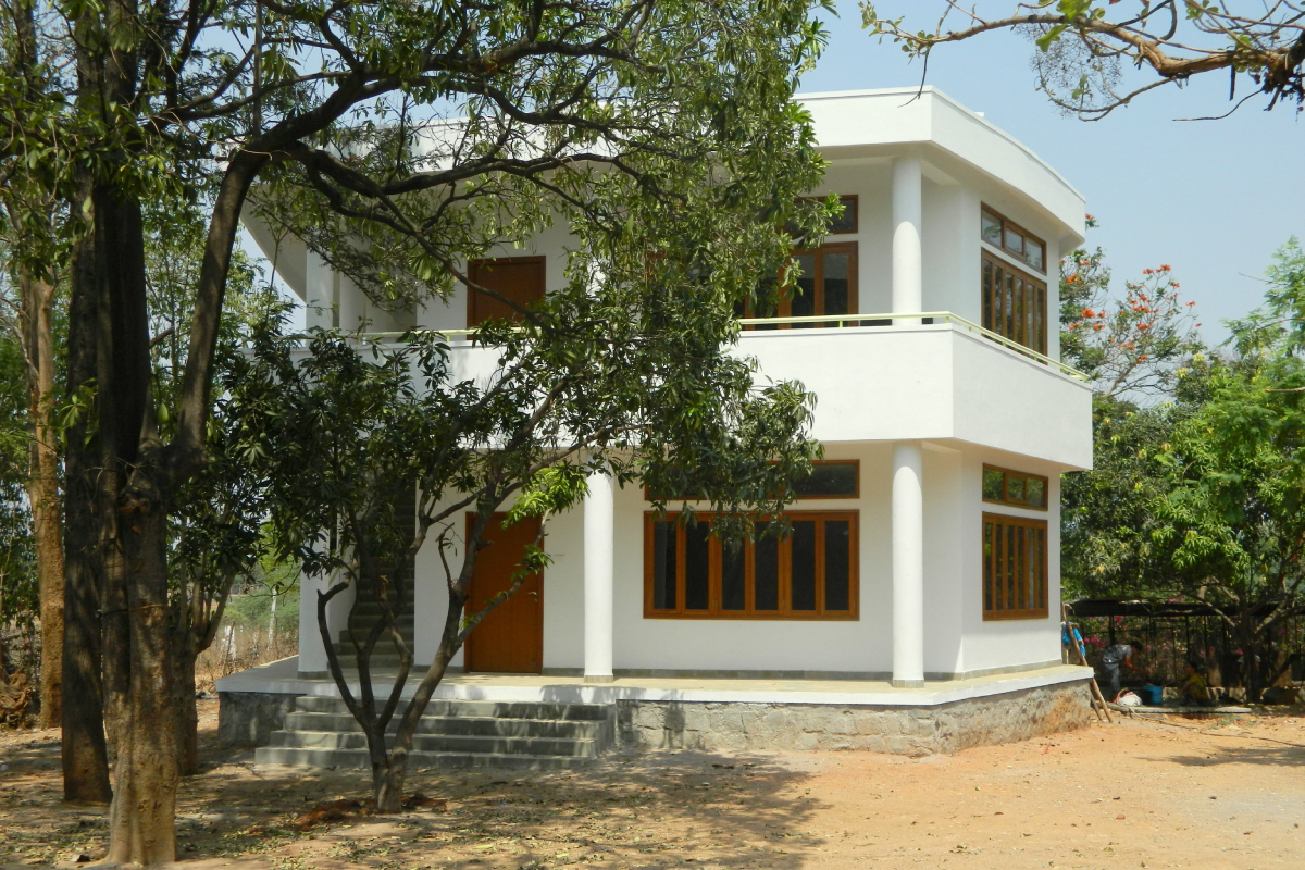 A two storey building within the Sloka campus, painted white, with trees in front of and behind it.