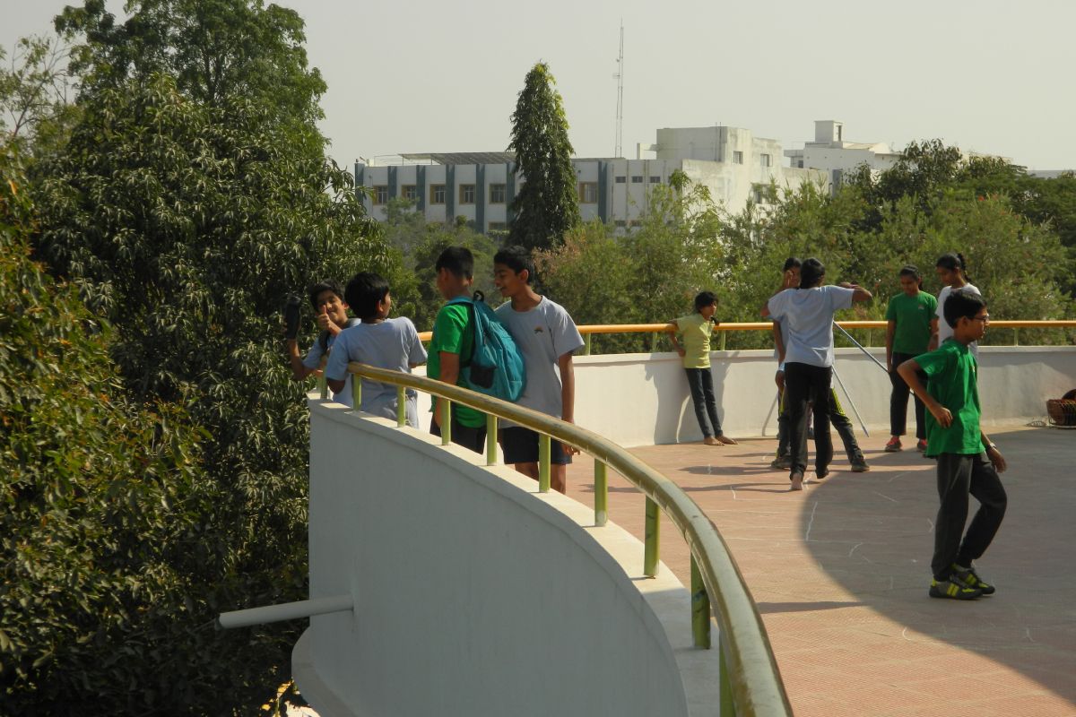 Students hanging out on the roof of the school building on a bright, sunlit day.