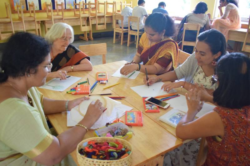 A group of teachers sit around a table involved in art and crafts work at a teacher training session.