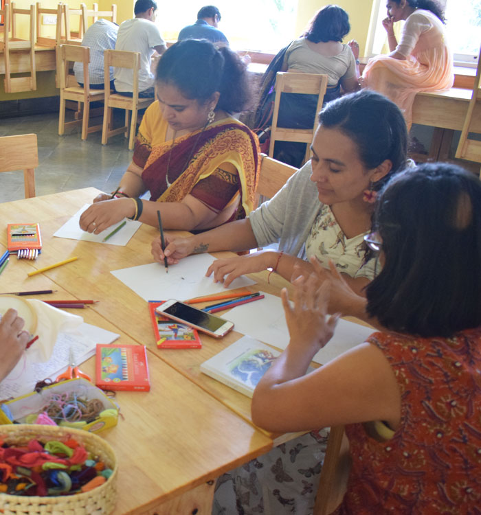 A group of teachers sit around a table involved in art and crafts work at a teacher training session.