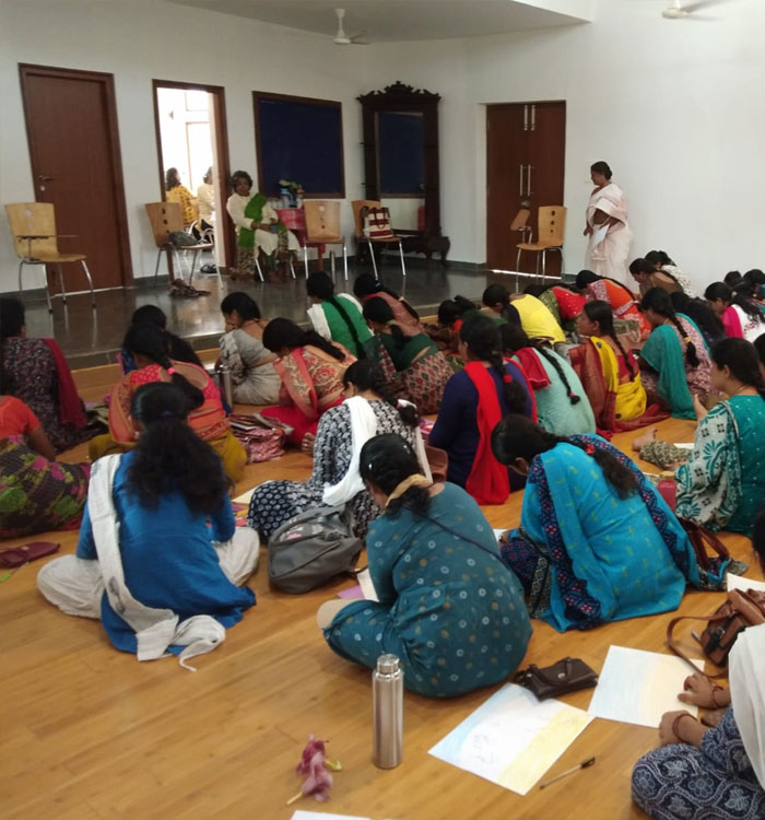 Several teachers sit on the floor taking notes during a tribal teacher training workshop at Sloka.