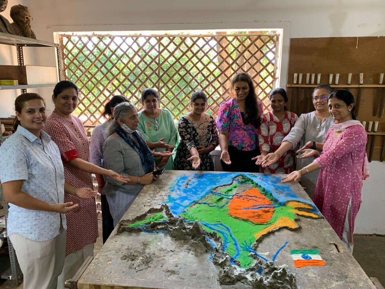 A group of teachers pose next to a model of India sculpted on a table during a teachers’ workshop.